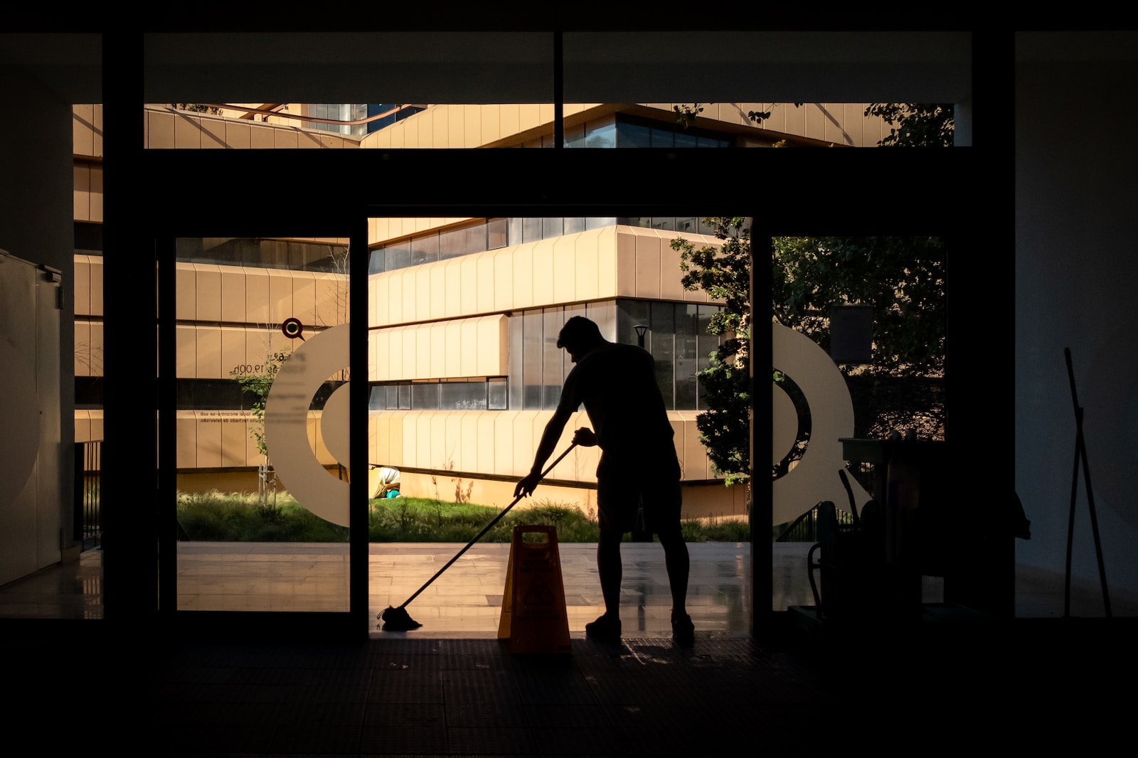 silhouette of man standing near glass window cleaning during daytime